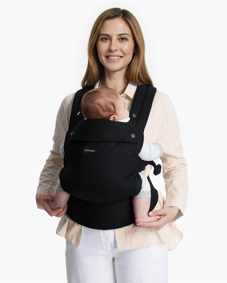 Translation missing: fr.Momcozy PureHug Baby Carrier. Black carrier, comfortable design, worn by mother holding baby. Ideal for babywearing